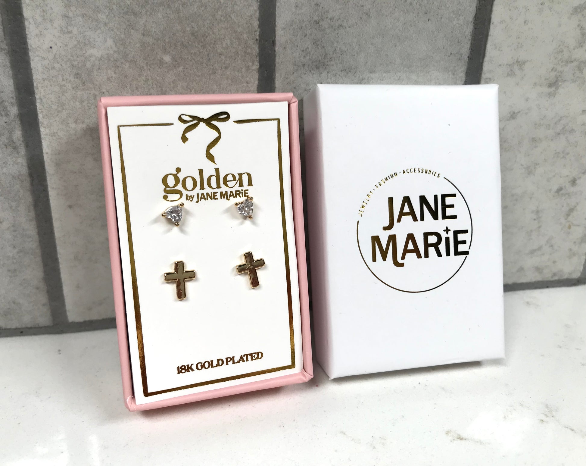 Kids 18K gold-plated stud earring set by Jane Marie, featuring crystal heart studs and small gold cross studs displayed in a pink gift box with white Jane Marie sleeve.