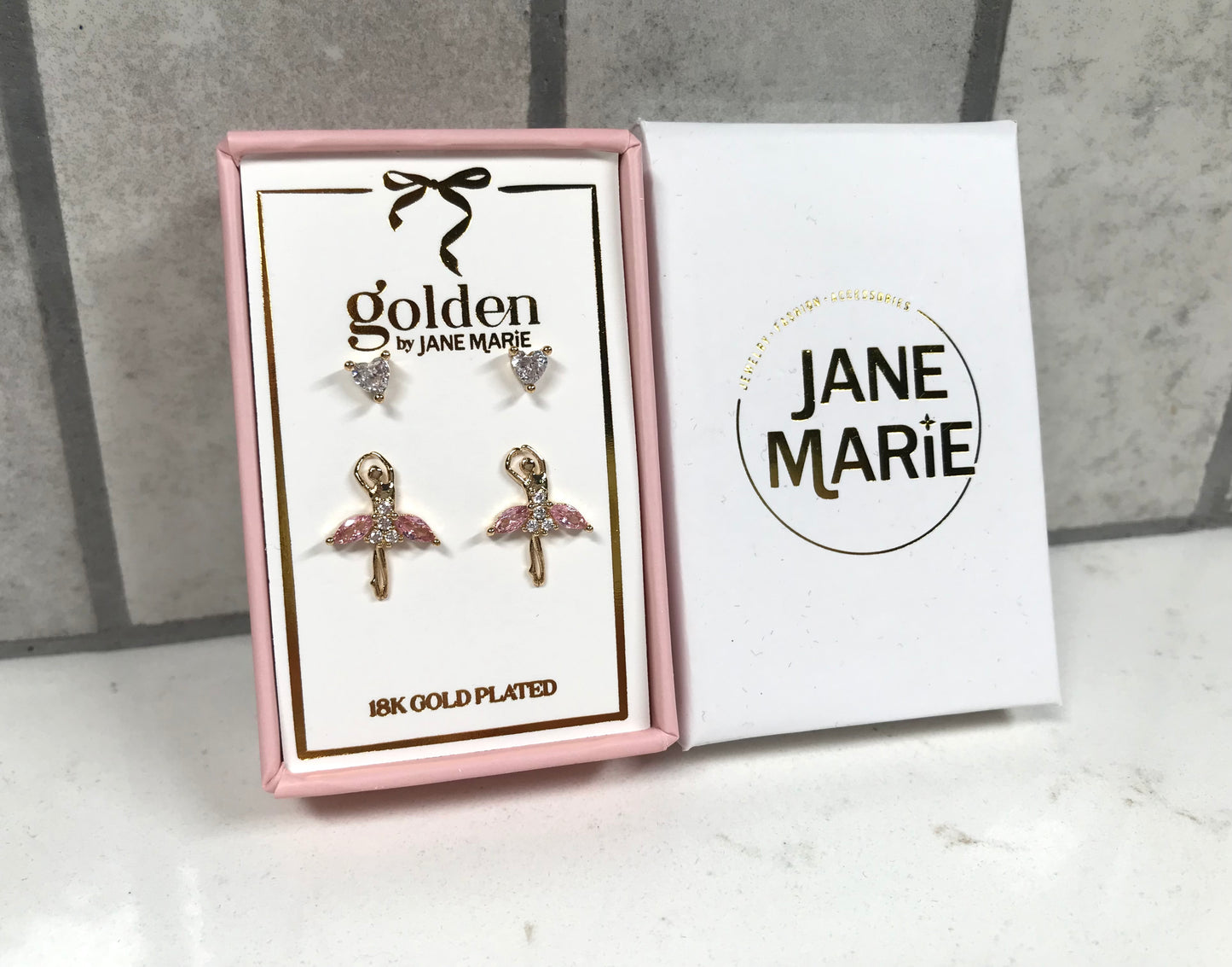 Kids 18K gold-plated earring set by Jane Marie featuring crystal heart studs and pink ballerina stud earrings, displayed in a pink jewelry box with a white Jane Marie sleeve.