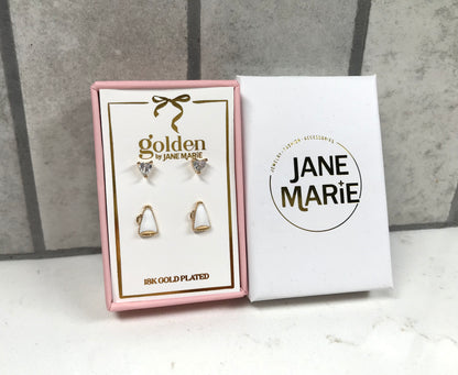 Kids 18K gold-plated earring set by Jane Marie with crystal heart studs and white megaphone studs, packaged in a pink jewelry box next to white Jane Marie sleeve.