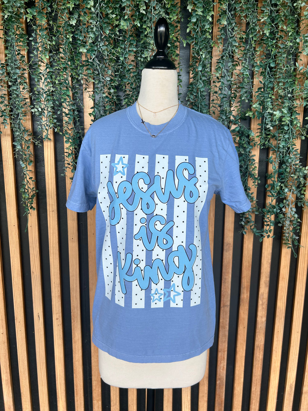 Washed denim  Jesus Is King Christian graphic tee displayed on mannequin with striped and polka dot design.