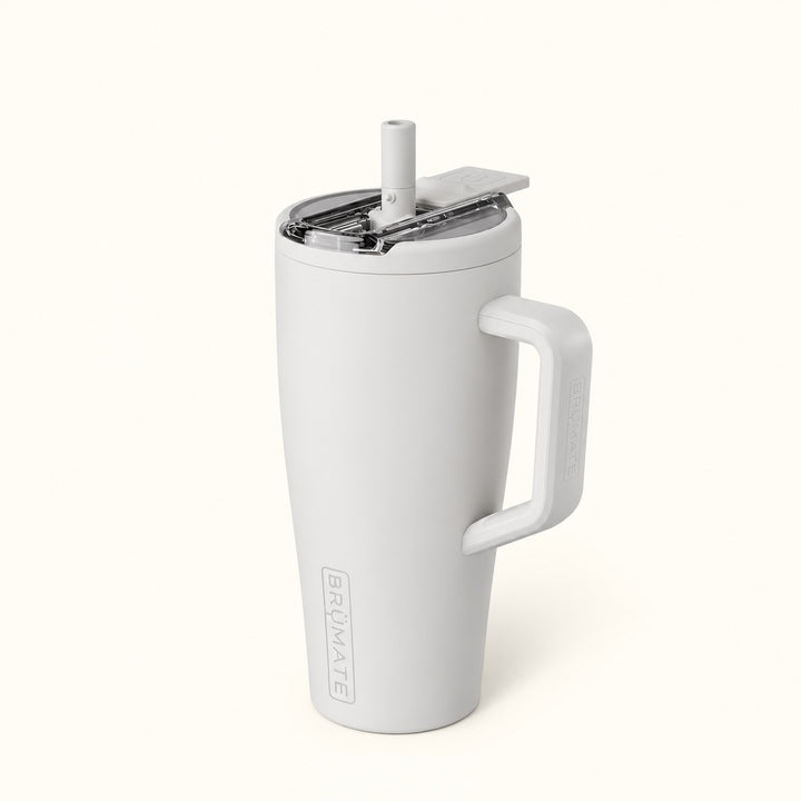 BrüMate Era Flip 30oz insulated straw tumbler in Dune featuring a soft matte light grey-beige finish, matching side handle, covered flip-down straw lid shown open, and vertical BrüMate branding. The compact 30oz leakproof water tumbler has a cupholder-friendly base and is displayed against a soft cream studio background.
