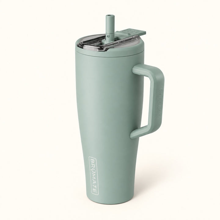 BrüMate Era Flip 40oz insulated straw tumbler in Sage featuring a soft matte muted sage green finish, large coordinating side handle, covered flip-down straw lid shown open, and vertical white BrüMate branding. The tall 40oz leakproof water tumbler has a cupholder-friendly base and is displayed against a soft cream studio background.