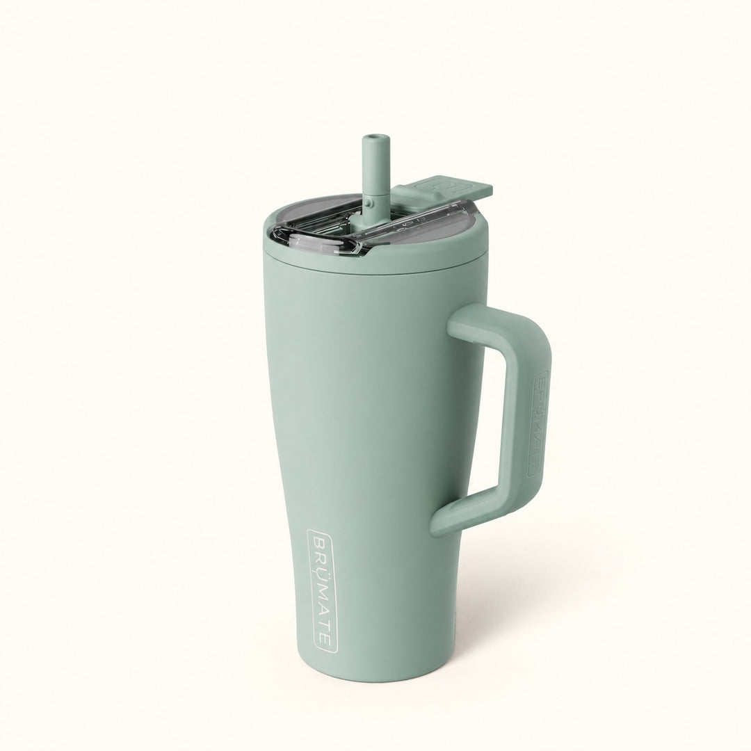 BrüMate Era Flip 30oz insulated straw tumbler in Sage featuring a soft matte sage green finish, matching carrying handle, covered flip-down straw lid shown open, and vertical white BrüMate branding. The compact 30oz leakproof water tumbler has a cupholder-friendly base and is displayed against a soft cream studio background.
