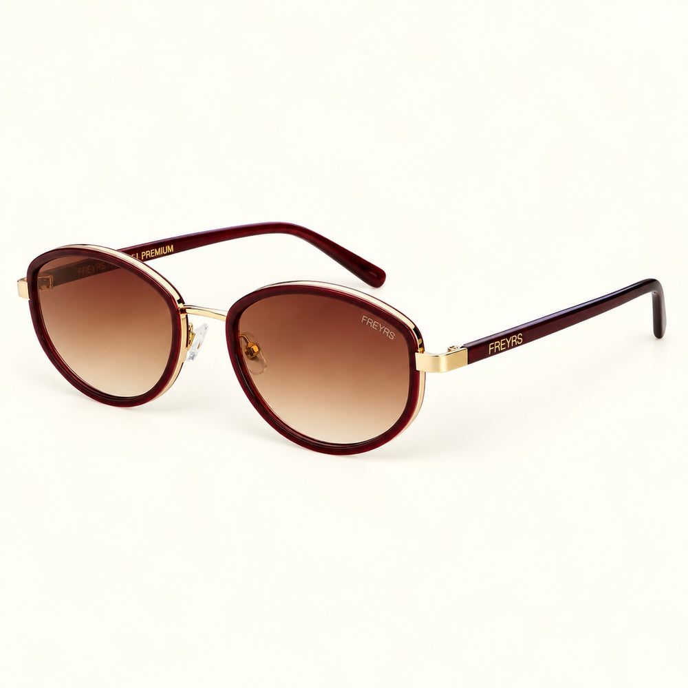 Angled view of FREYRS Jordan burgundy oval sunglasses showing handmade acetate frames, brown gradient lenses, gold-tone accents, and burgundy temples.