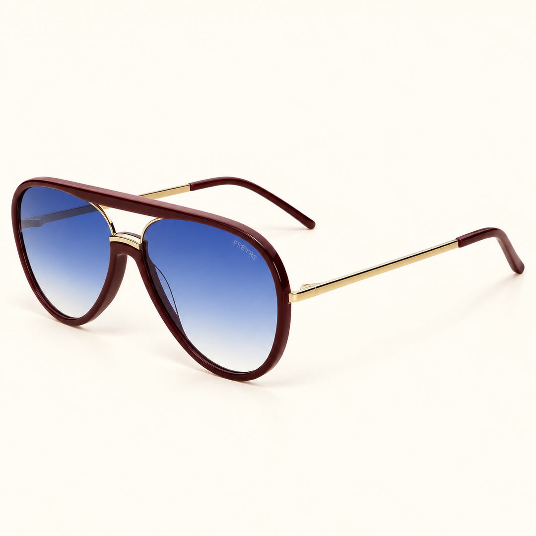 Angled view of FREYRS Shay Burgundy aviator sunglasses showing biodegradable burgundy acetate frames, blue gradient lenses, slim gold-tone temples, and matching burgundy tips.
