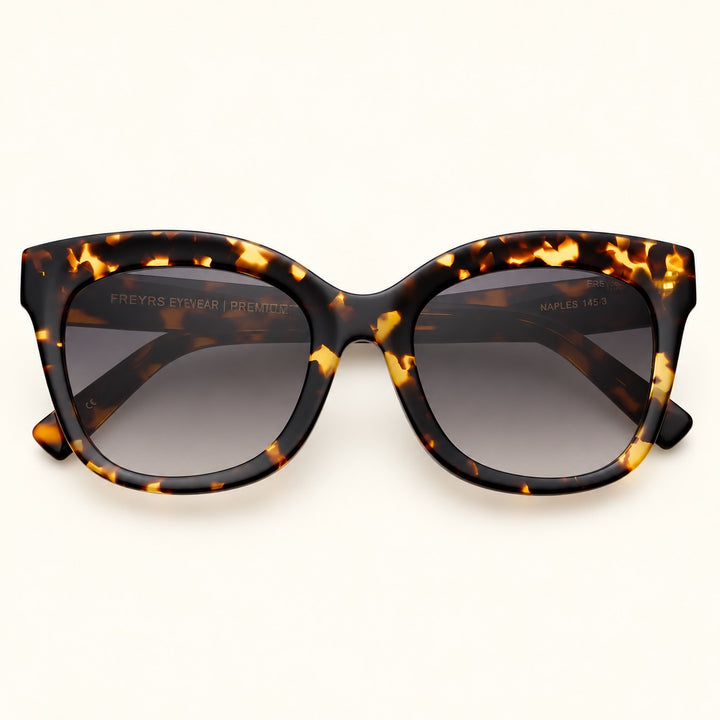 Angled view of FREYRS Naples Cat Eye Sunglasses in Tortoise featuring bold brown and amber acetate frames, smoky gray gradient lenses, and wide tortoiseshell temples.