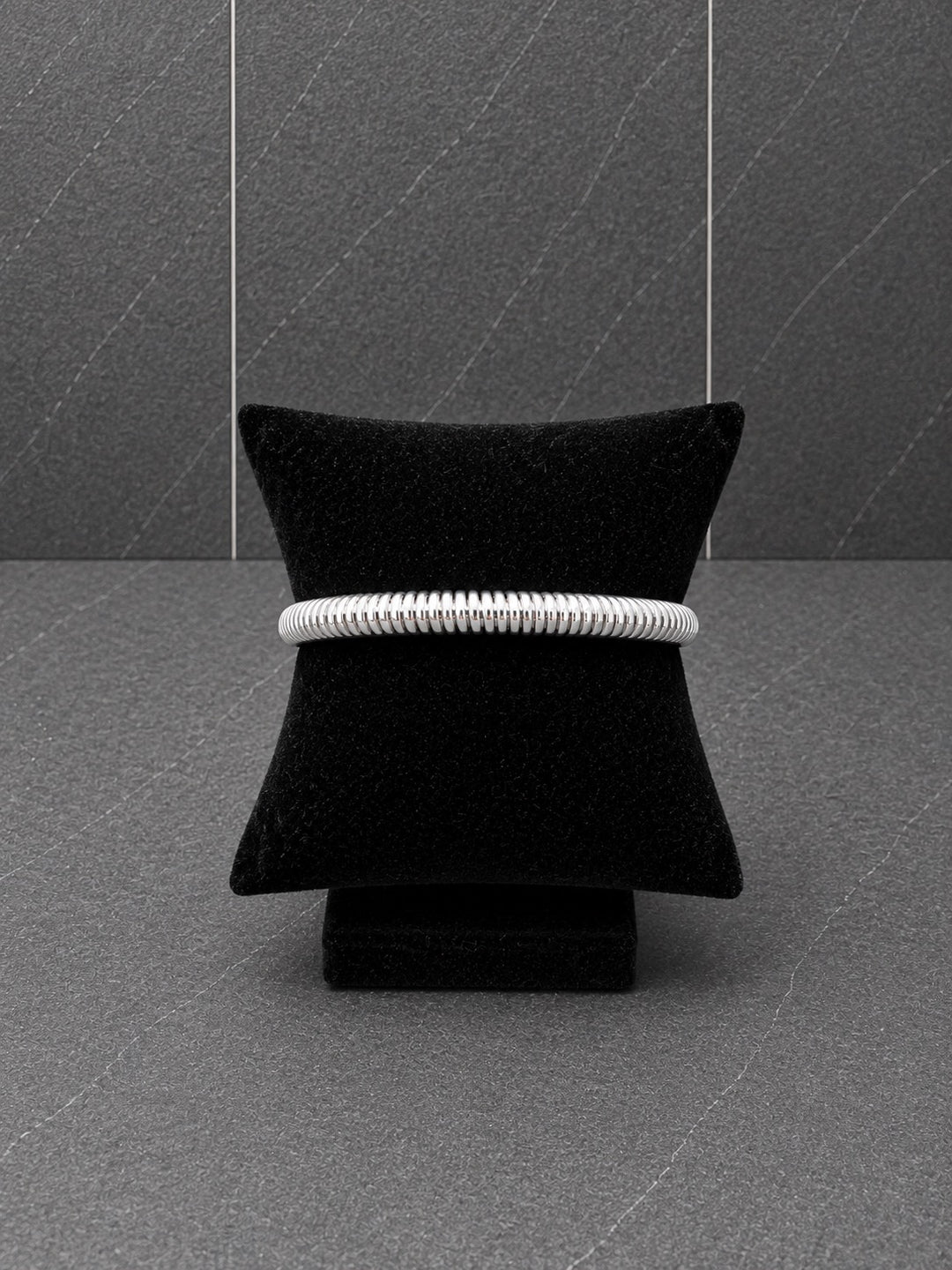 Silver-plated textured ribbed bangle bracelet displayed on a black velvet bracelet pillow.