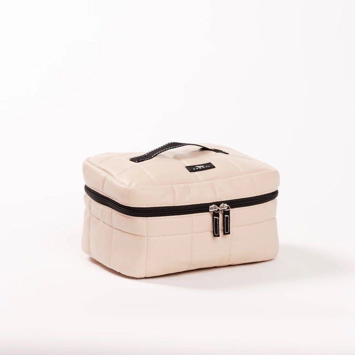 A cream-colored quilted cosmetic bag with black trim, dual zipper pulls, and a top handle, set against a plain white background.