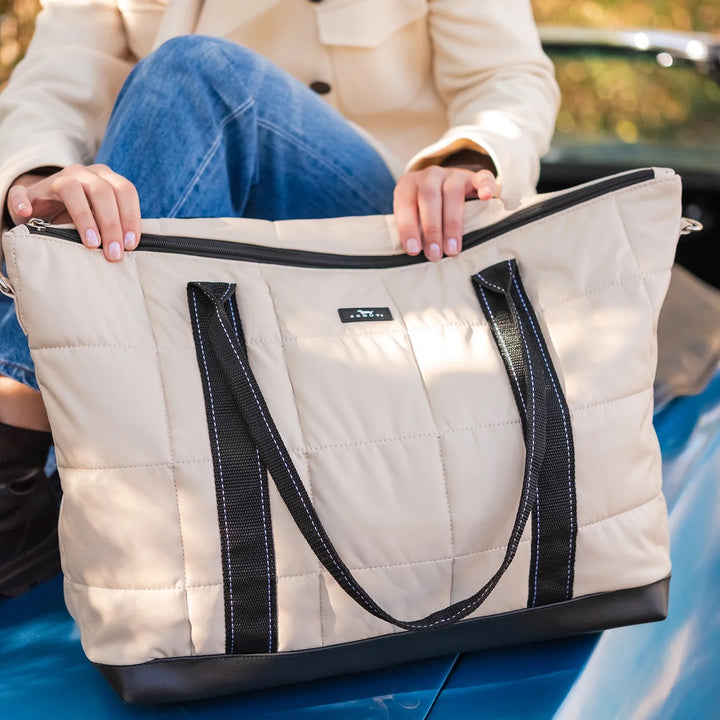 Person holding a beige quilted tote bag with black handles and trim.