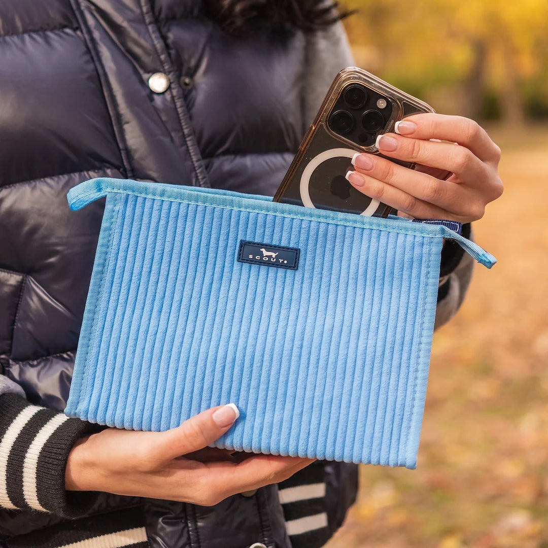 Person holding a blue textured pouch with a phone, wearing a dark jacket outdoors.