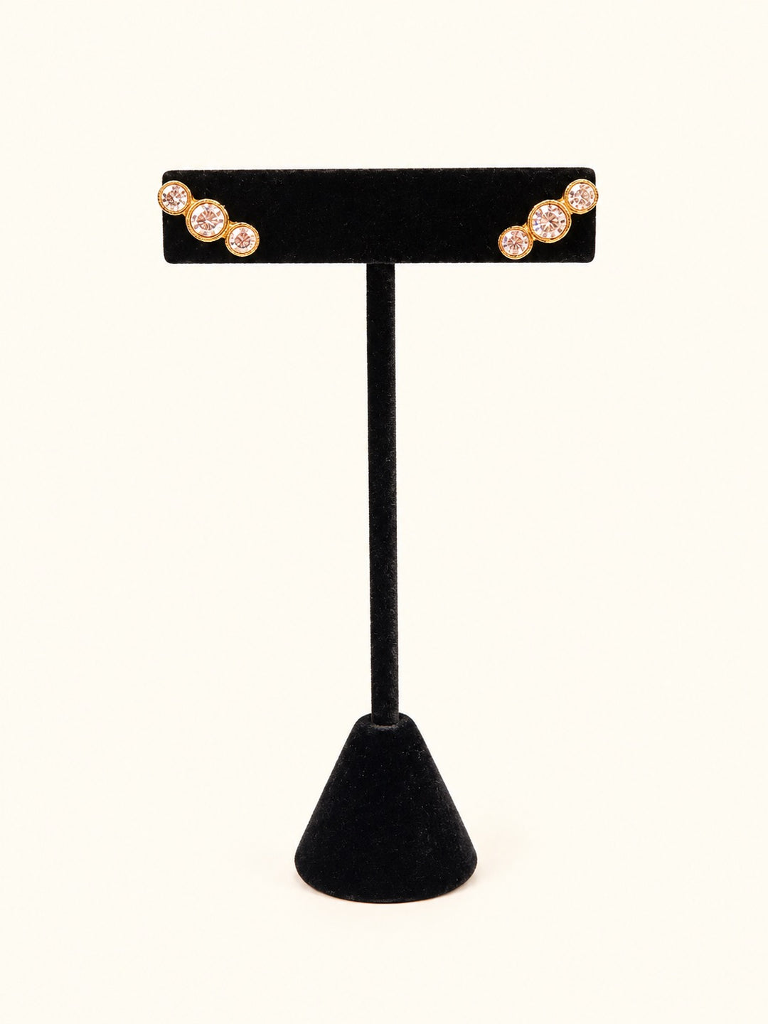 Lyric Gold Earrings featuring three graduated sparkling clear stones in an 18K gold plated stainless steel setting, displayed on a black velvet jewelry stand.