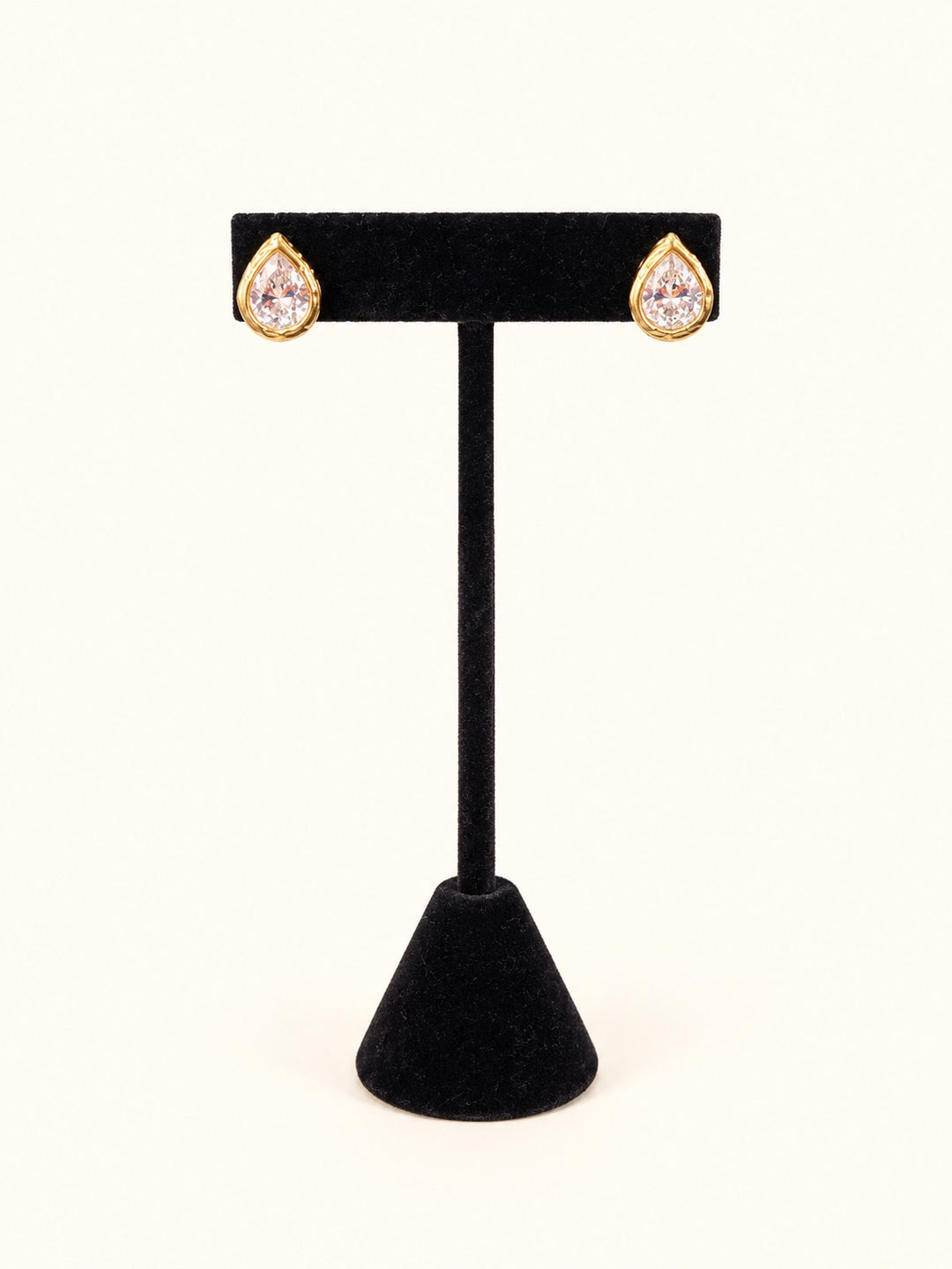 Tessa Gold Teardrop Stud Earrings featuring sparkling pear-shaped clear stones in 18K gold plated stainless steel settings, displayed on a black velvet jewelry stand.