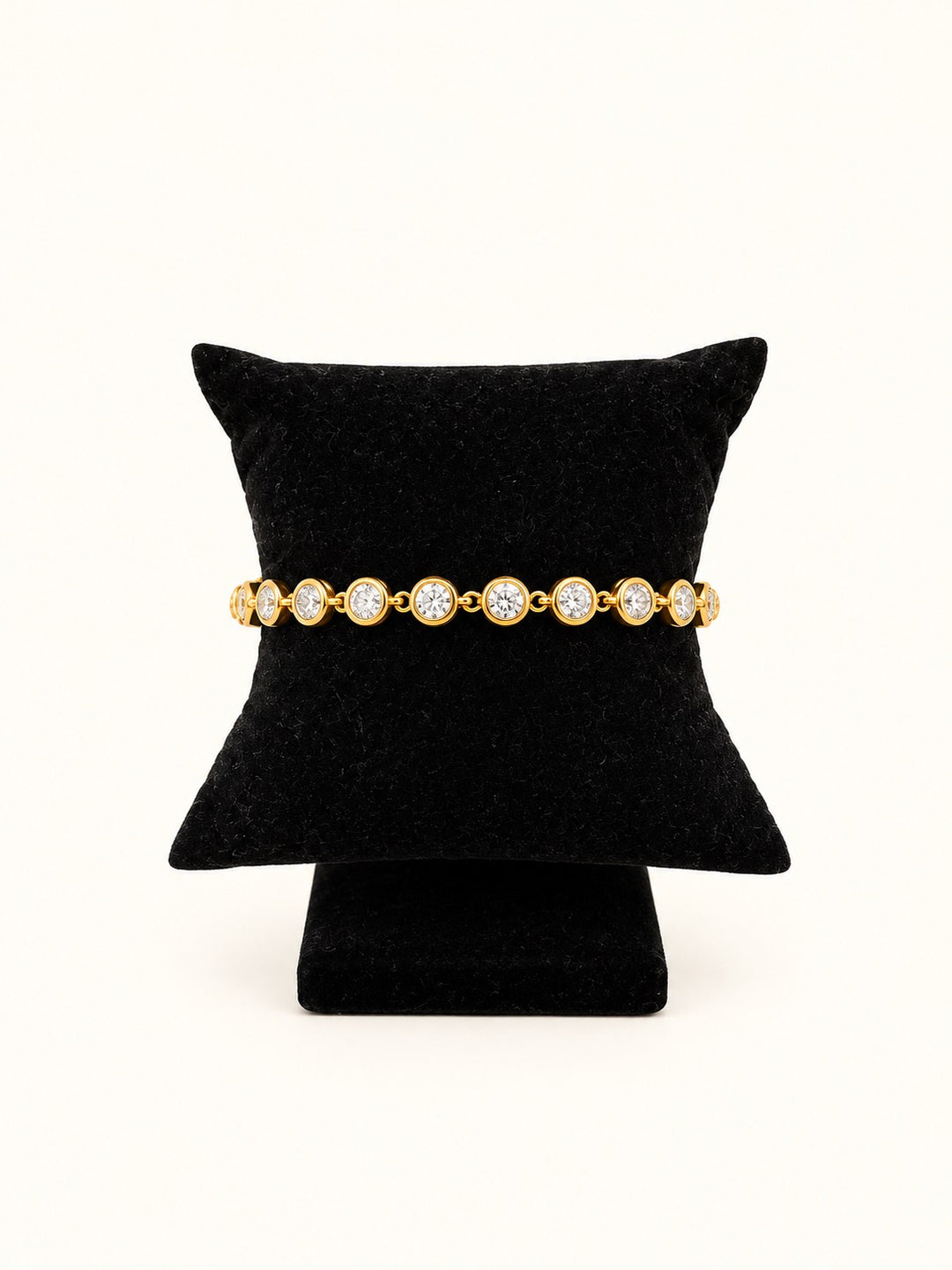 Roxie Gold Tennis Bracelet featuring round sparkling clear stones in 18K gold plated bezel settings, displayed on a black velvet jewelry pillow.