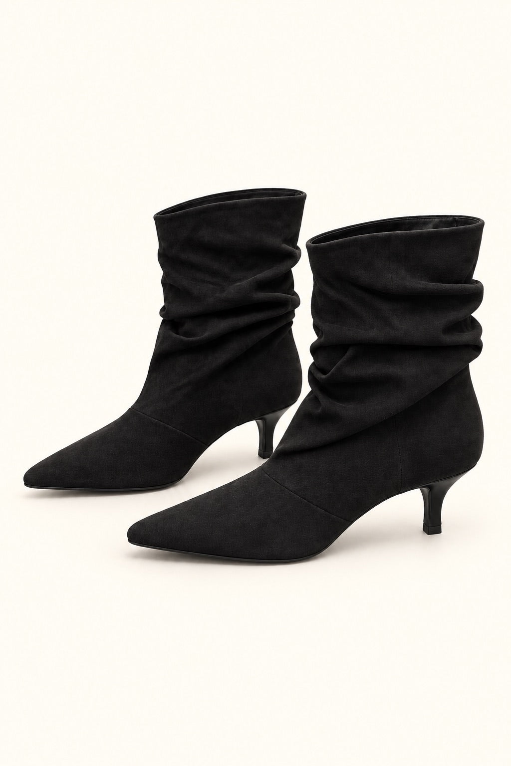 Angled view of black faux-suede slouch ankle boots with pointed toes and kitten heels.