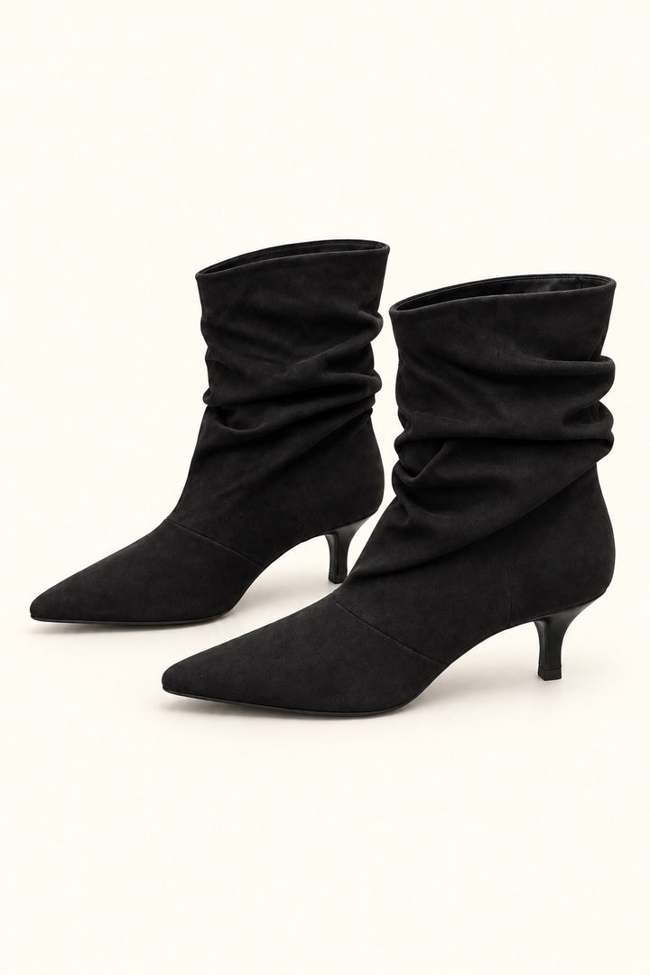 Angled view of black faux-suede slouch ankle boots with pointed toes and kitten heels.