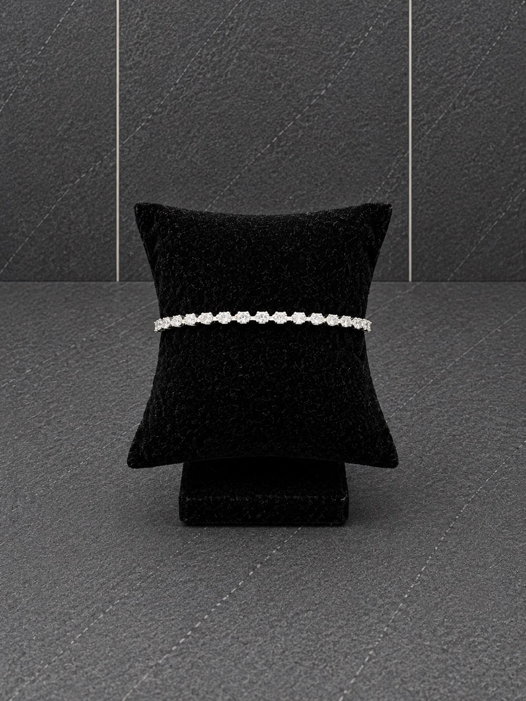Silver-plated tennis bracelet featuring a continuous row of sparkling cubic zirconia stones displayed on a black velvet bracelet pillow.