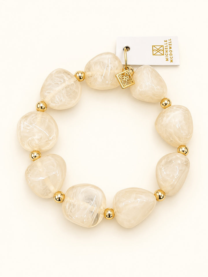 Lindon Cream Statement Bracelet with glossy ivory marbled resin beads, gold-tone spacers, and decorative charm photographed on a cream background.