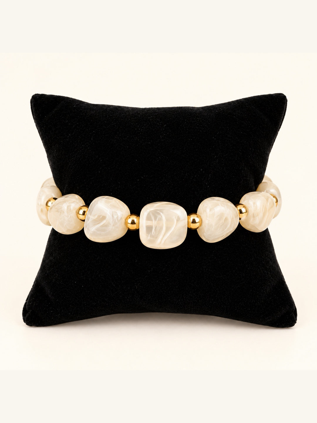 Lindon Cream Beaded Stretch Bracelet featuring oversized ivory marbled resin beads and polished gold-tone spacers displayed on a black velvet pillow.