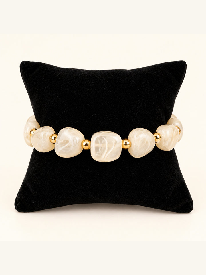 Lindon Cream Beaded Stretch Bracelet featuring oversized ivory marbled resin beads and polished gold-tone spacers displayed on a black velvet pillow.