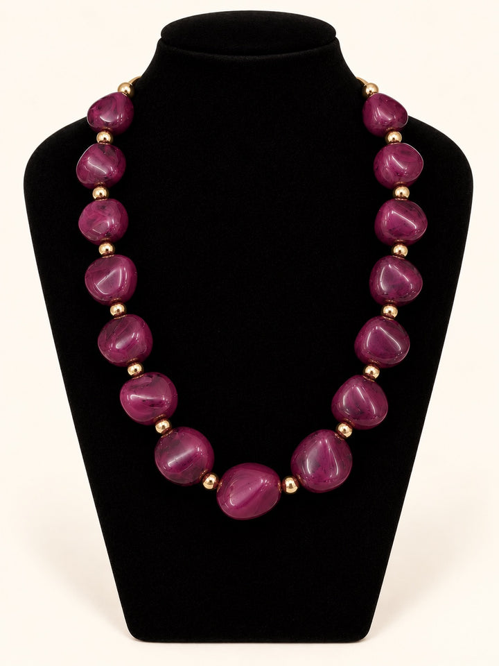 Lindon Plum Statement Necklace featuring oversized glossy plum resin beads and polished gold-tone spacers on a black velvet jewelry display.