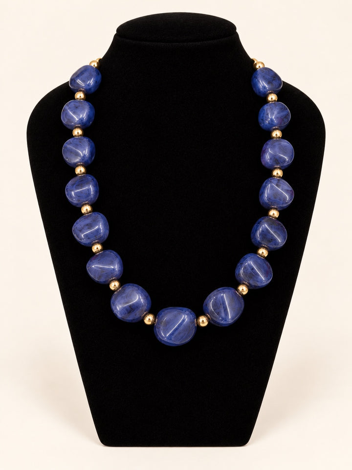 Lindon Blue Statement Beaded Necklace featuring vibrant cobalt blue resin beads and gold-tone spacer accents displayed on black velvet.