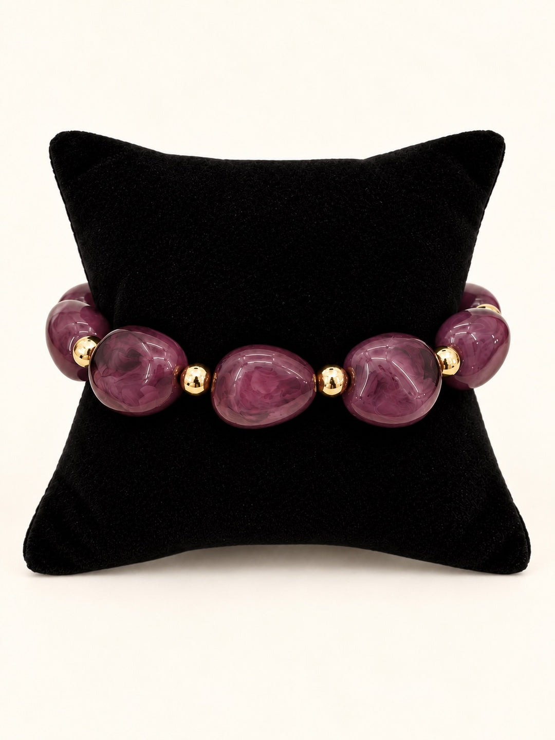 Lindon Plum Beaded Statement Bracelet featuring oversized glossy plum resin beads with gold-tone spacers displayed on a black velvet jewelry pillow.