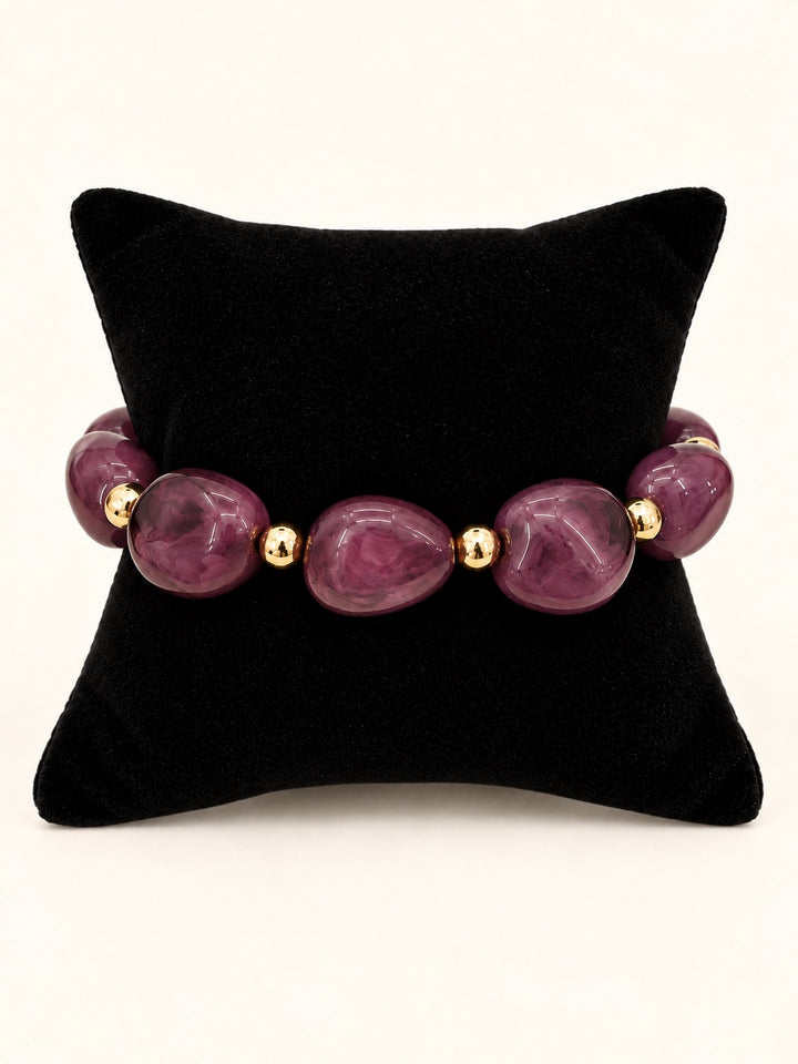 Lindon Plum Beaded Statement Bracelet featuring oversized glossy plum resin beads with gold-tone spacers displayed on a black velvet jewelry pillow.