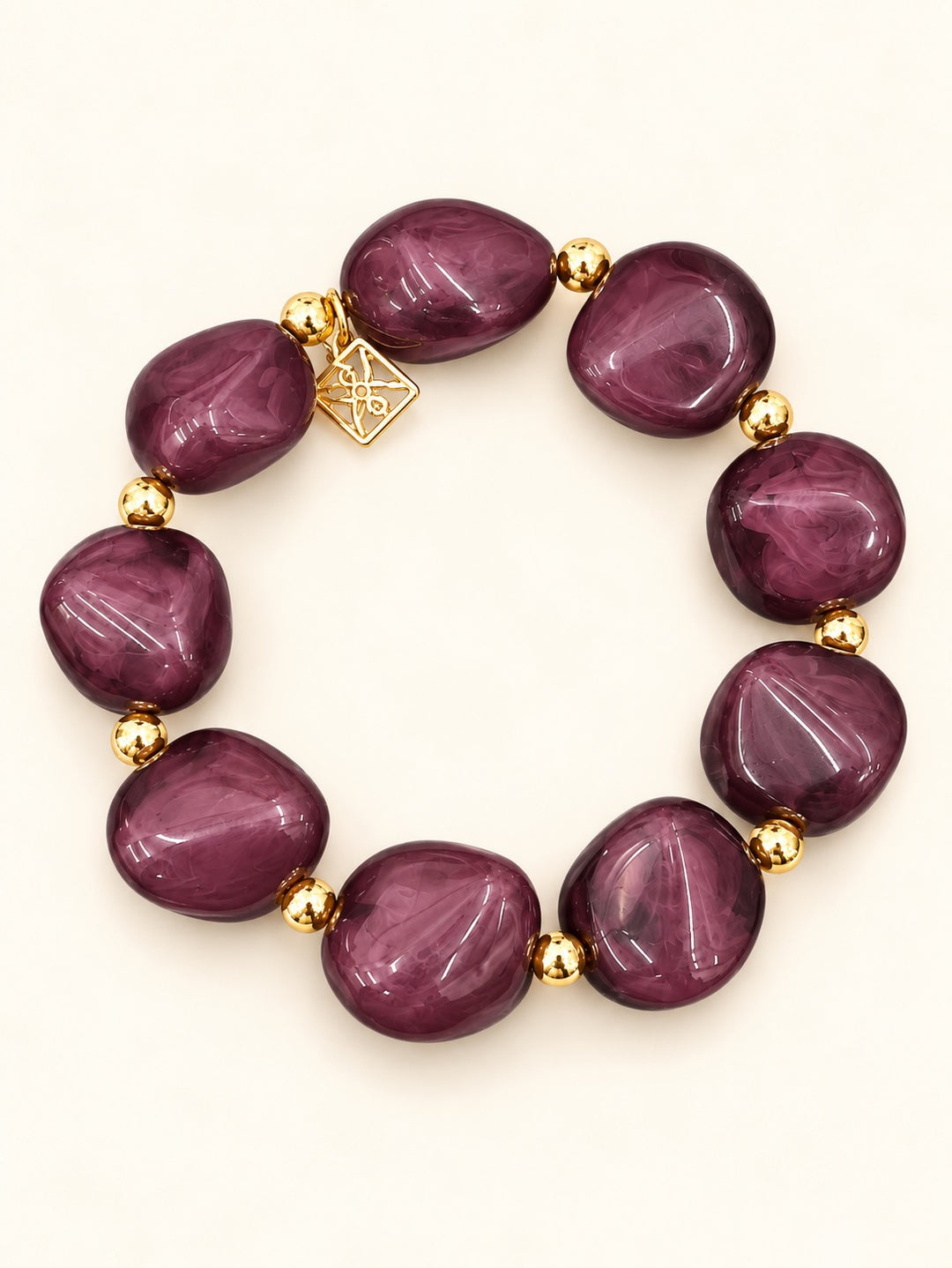 Lindon Plum Stretch Bracelet with chunky purple-pink marbled resin beads, polished gold-tone accents, and decorative charm on a cream background.