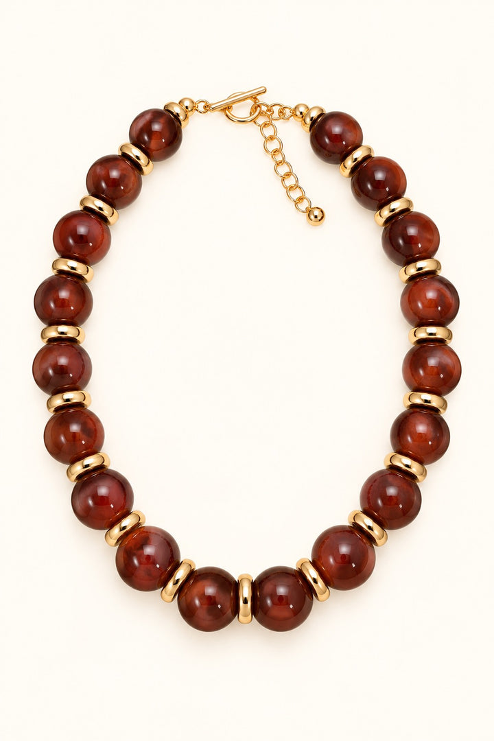 Sellah Olive Beaded Statement Necklace featuring golden-olive resin beads, gold-tone ring spacers, and adjustable extender chain photographed on a cream background.