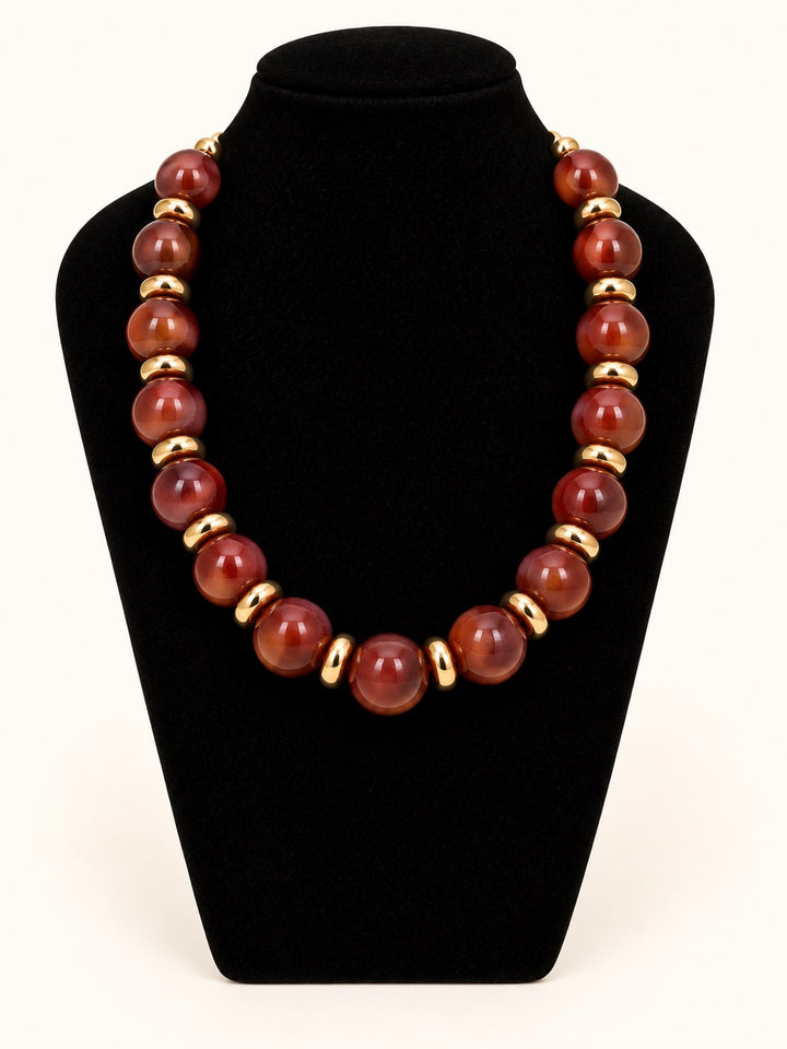 Michelle McDowell Sellah Necklace in Olive featuring oversized translucent golden-olive resin beads and shiny gold-tone spacers displayed on a black velvet necklace stand.