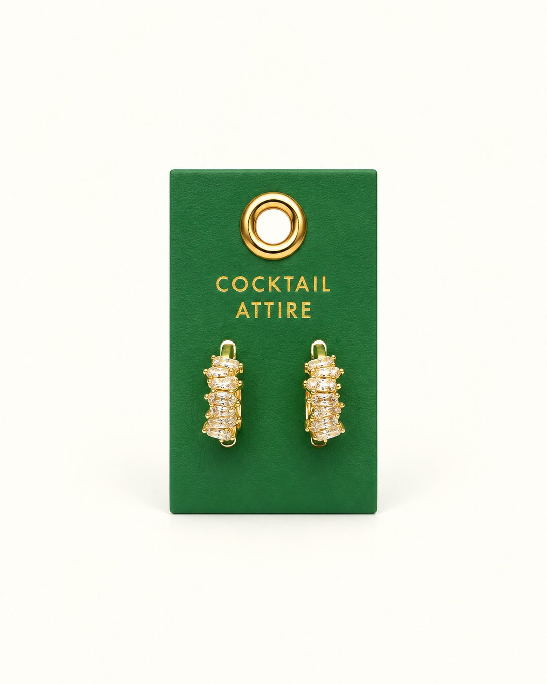 Gold-tone huggie hoop earrings with faceted clear glass crystals and rhinestone accents displayed on a green Cocktail Attire Palm Beach leather jewelry tab.