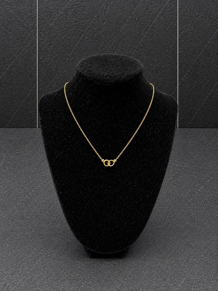 A delicate gold chain necklace with a double interlocking ring pendant, displayed on a black velvet jewelry bust against a dark gray textured background.