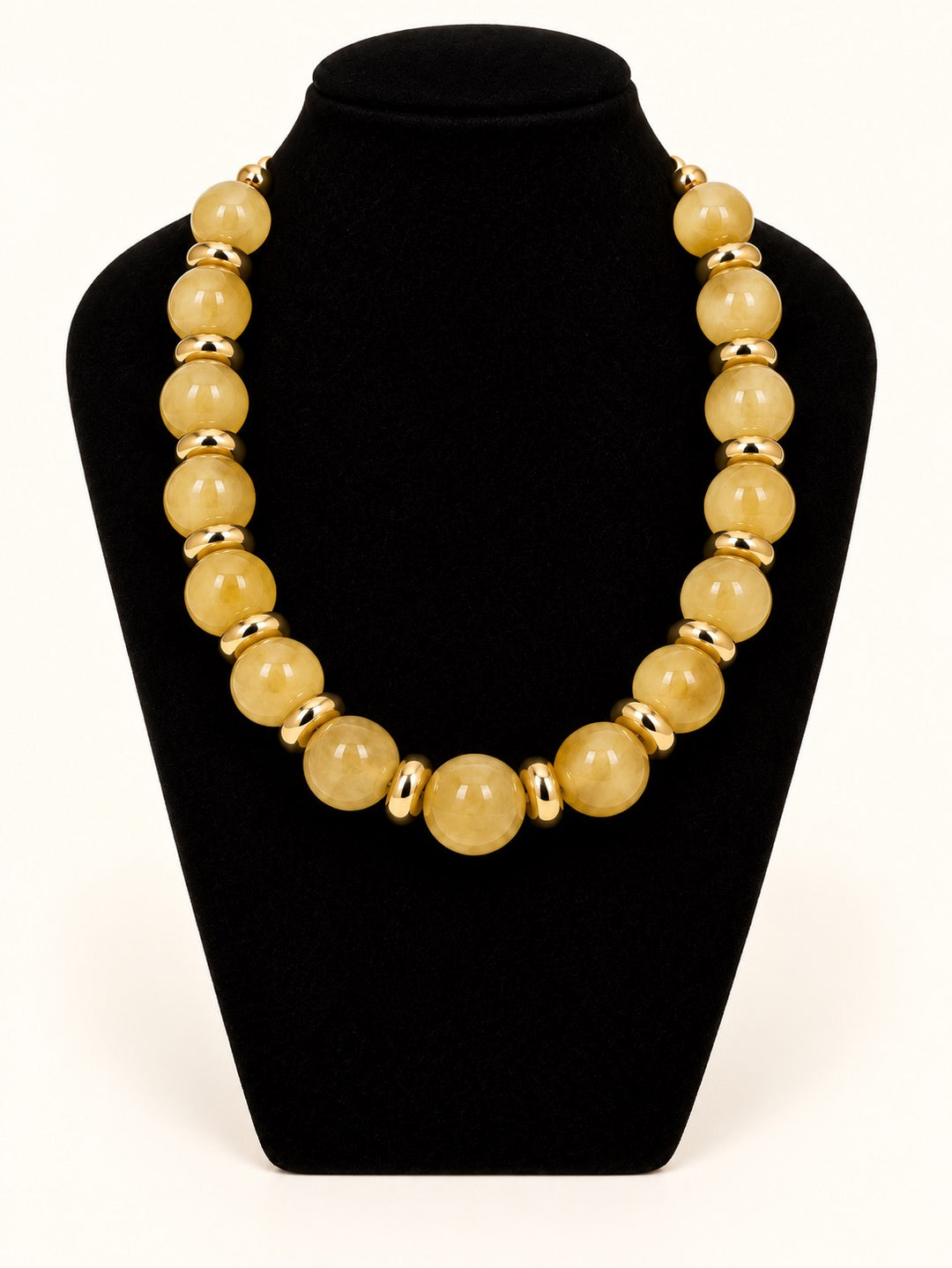 Michelle McDowell Sellah Necklace in Olive featuring oversized translucent golden-olive resin beads and shiny gold-tone spacers displayed on a black velvet necklace stand.