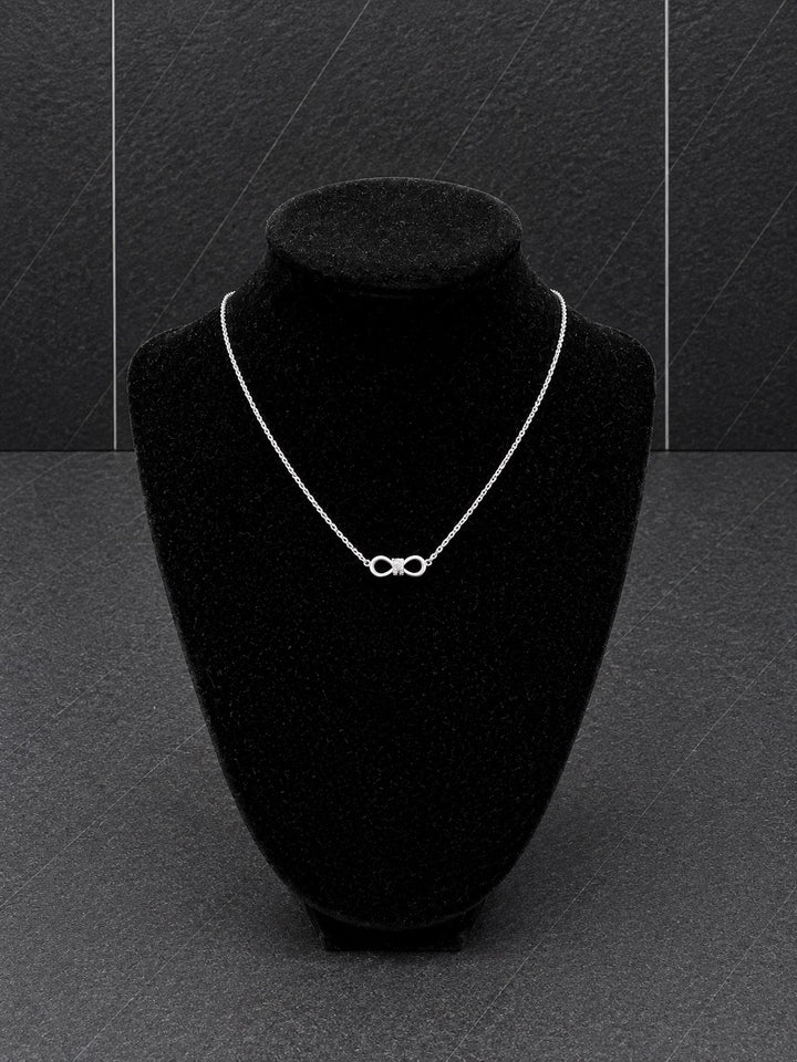 A delicate silver infinity necklace displayed on a black velvet jewelry bust against a dark gray textured background.