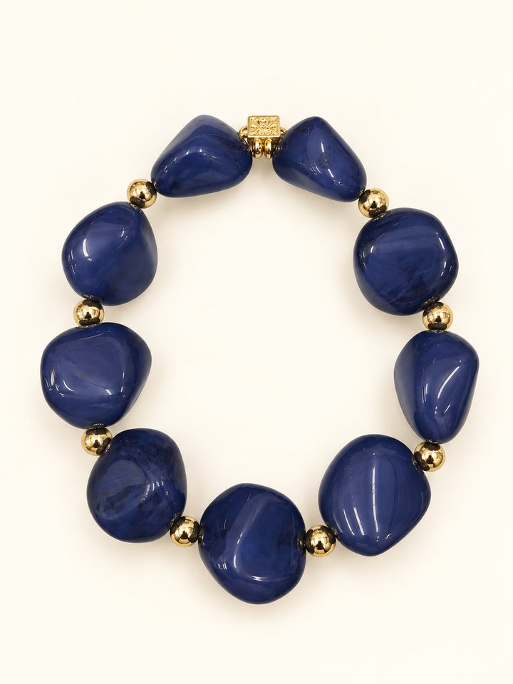 Lindon Blue Stretch Bracelet with oversized glossy cobalt blue marbled resin beads, gold-tone spacers, and decorative charm photographed on a cream background.