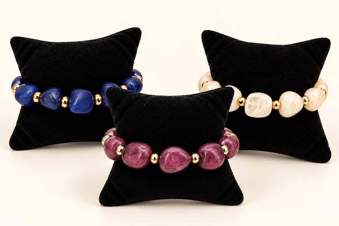 Lindon Beaded Statement Bracelets in Cream, Plum, and Blue featuring chunky resin beads and gold-tone accents displayed on black velvet jewelry pillows.