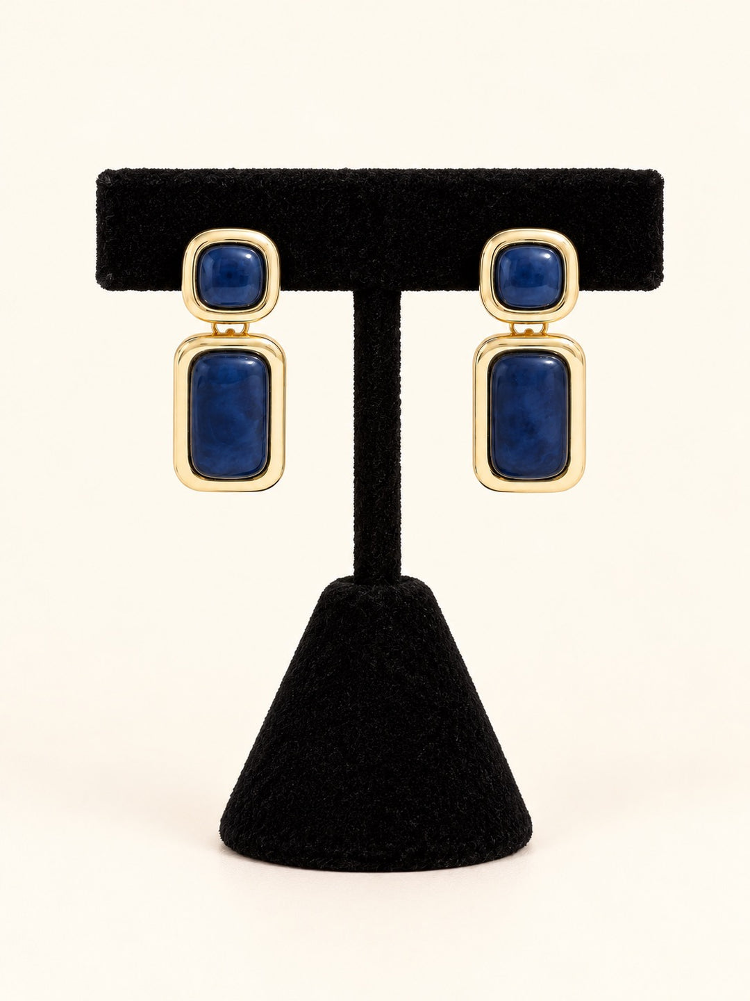 Laurel Earrings in Blue featuring deep navy blue resin accents and polished gold-tone geometric settings displayed on a black velvet jewelry stand.