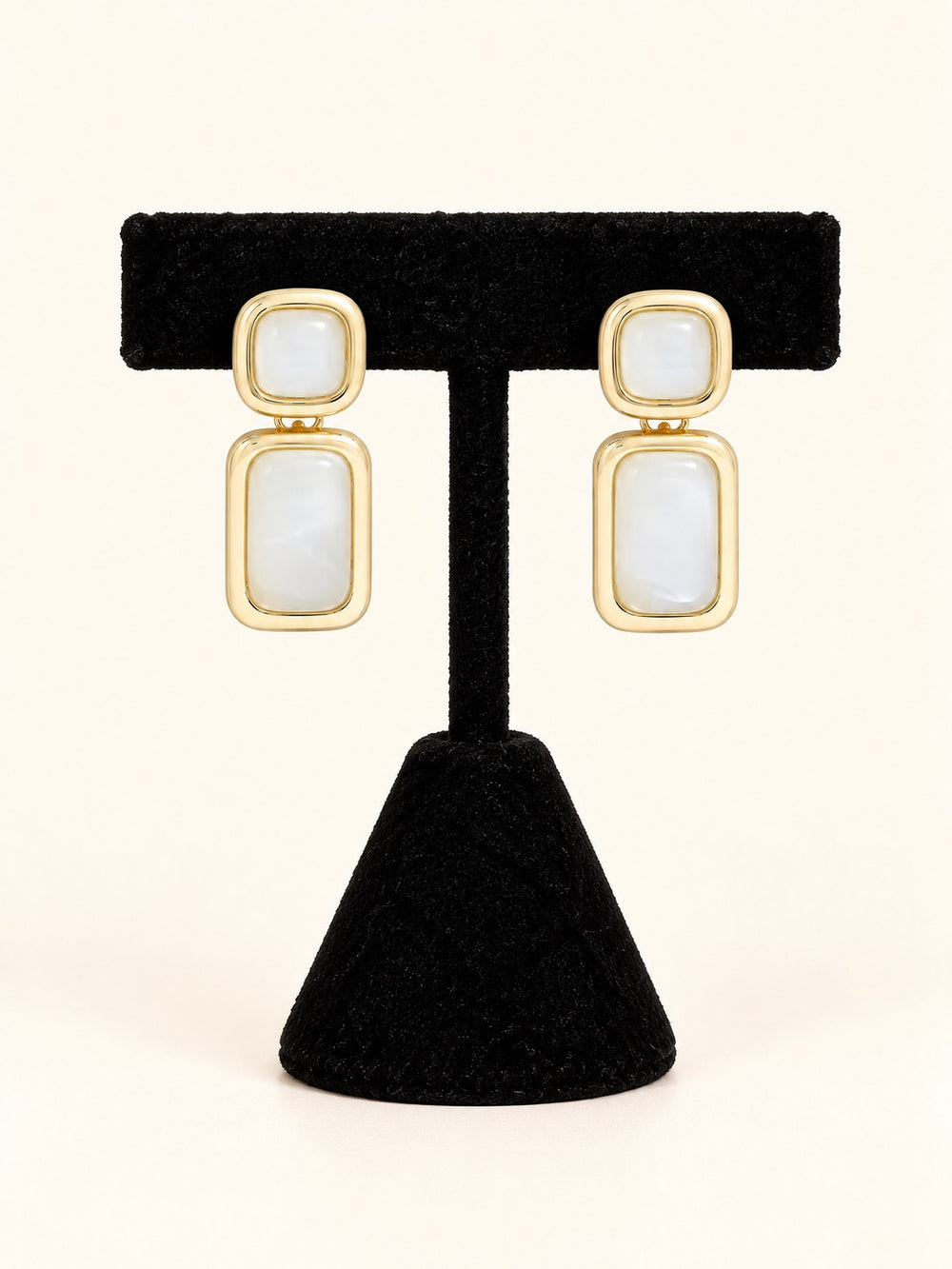 Laurel Earrings in Cream featuring glossy ivory-white resin accents, polished gold-tone frames, and geometric drop design on a black velvet stand.