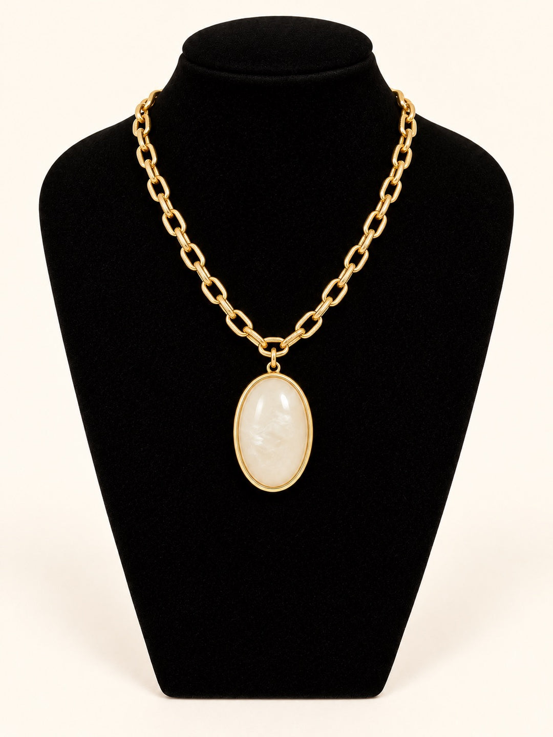 Susannah Pendant Necklace featuring a cream marbled oval pendant framed in polished gold-tone metal with a textured gold chain, displayed on a black velvet necklace stand at Square 1 Boutique.