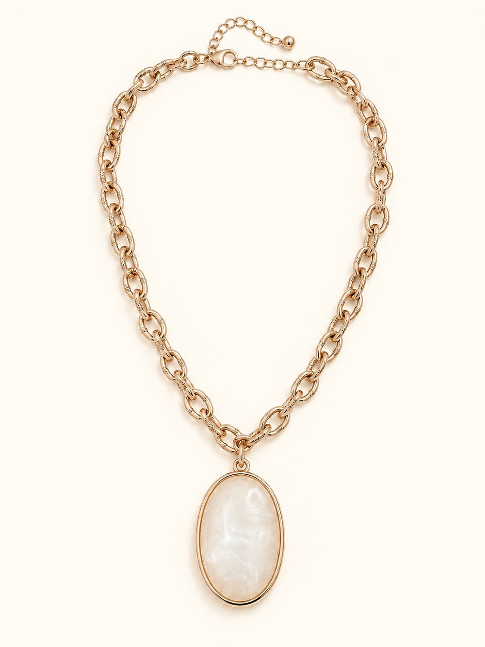 Susannah Gold Pendant Necklace laid flat on a cream background, showcasing its oval cream pendant, textured gold-tone chain, lobster clasp, and adjustable extender.