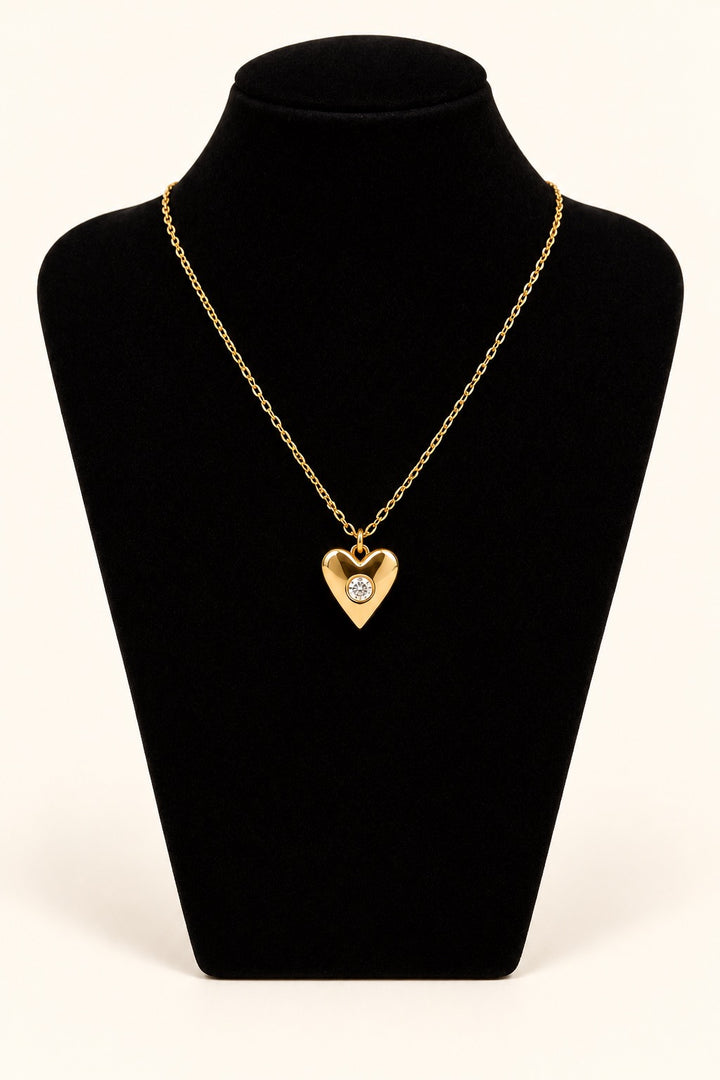 Michelle McDowell Loved Chain Necklace featuring an 18K gold-plated heart pendant with a sparkling clear center stone on a delicate gold chain, displayed on black velvet at Square 1 Boutique.