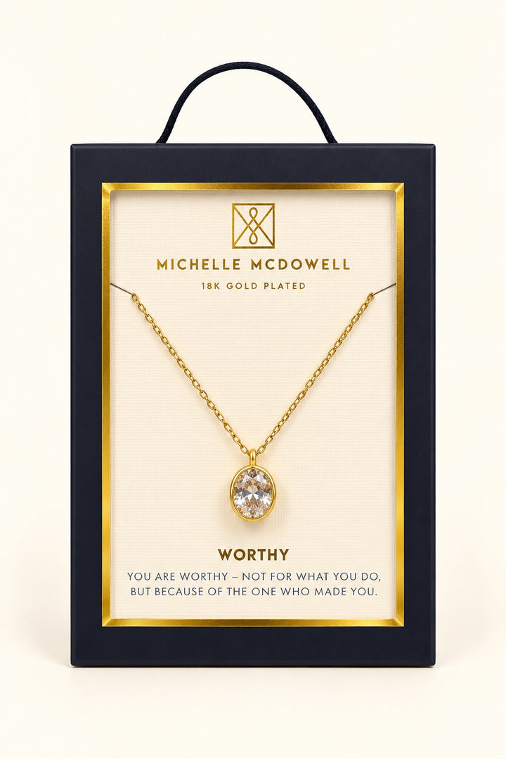 Michelle McDowell Valued Gold Pendant Necklace in branded gift packaging with a Worthy inspirational sentiment card, featuring an oval clear stone pendant and delicate gold-plated chain.