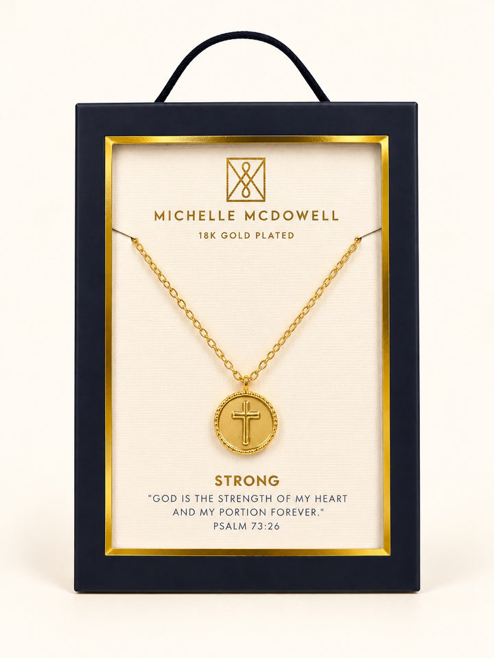 Michelle McDowell Saved Gold Cross Necklace in branded gift packaging featuring an 18K gold-plated chain, round cross pendant, and Strong inspirational scripture card with Psalm 73:26.