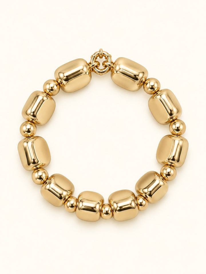 Rosalie Small Gold Beaded Bracelet featuring chunky rounded-square gold-tone beads with polished round spacer accents and a circular bracelet design on a cream studio background.