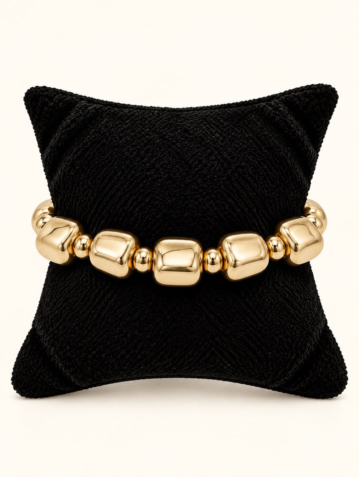 Rosalie Beaded Bracelet Small by Michelle McDowell featuring polished gold rounded-square beads and smaller gold spacers displayed on a black velvet jewelry pillow at Square 1 Boutique.