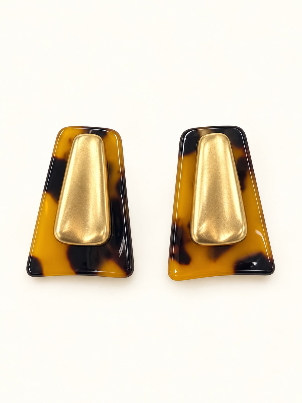 Close-up of Michelle McDowell Willa Tortoise Shell Earrings featuring glossy amber and dark brown geometric frames with brushed gold-tone center details on a cream studio background.