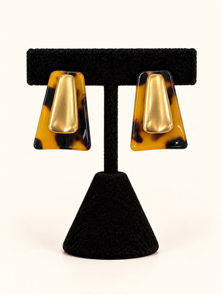 Willa Earrings by Michelle McDowell featuring amber and dark brown tortoise shell geometric statement earrings with brushed gold-tone center accents displayed on a black velvet earring stand at Square 1 Boutique.