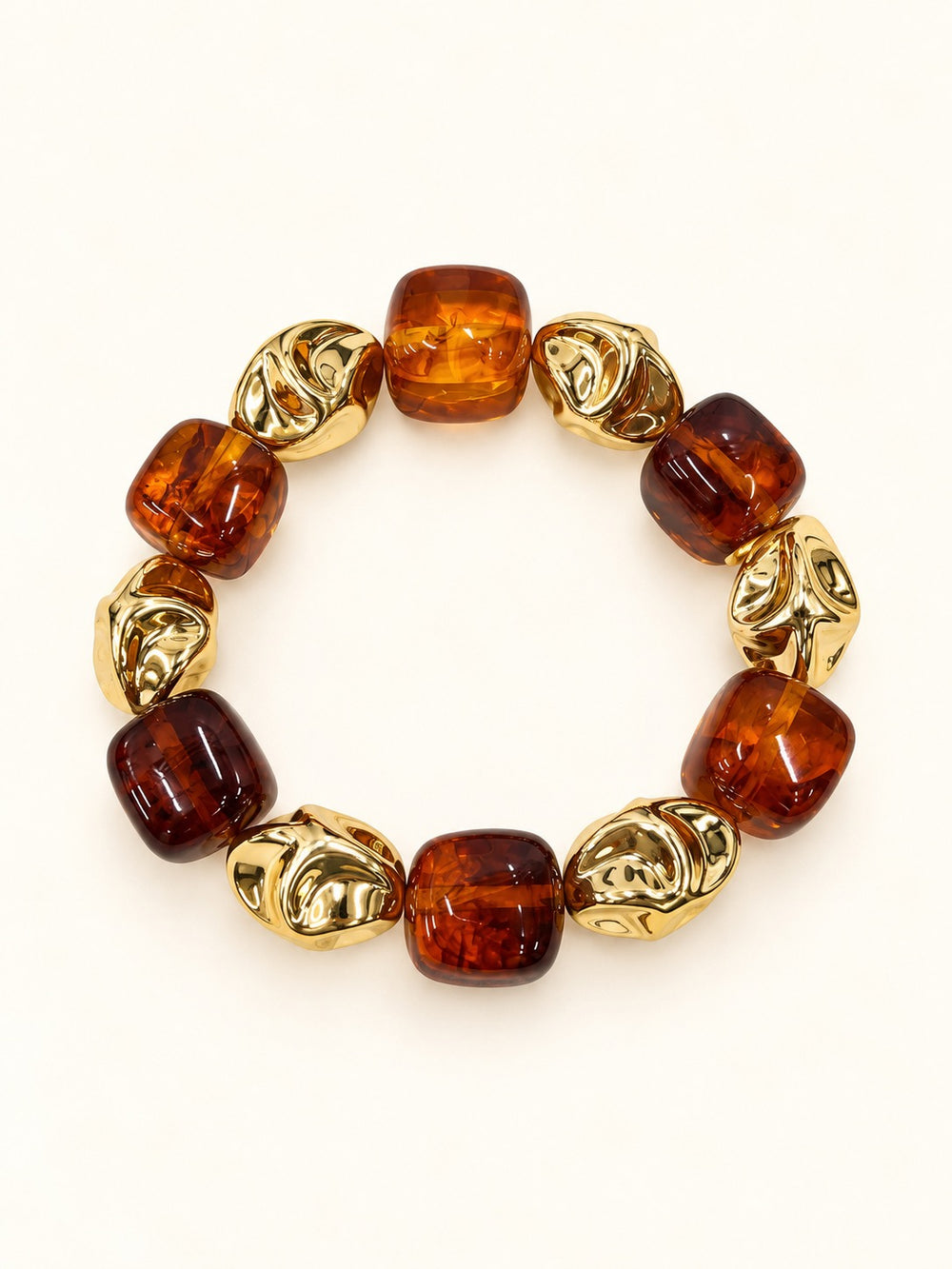 Layla Tortoise Beaded Stretch Bracelet displayed on a black velvet bracelet pillow, featuring glossy amber-brown translucent beads and textured gold-tone statement accents against a cream background.