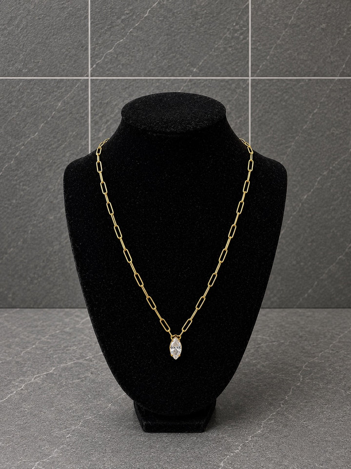 A gold chain necklace with a marquise-shaped clear gemstone pendant, displayed on a black velvet jewelry bust against a gray tiled background.