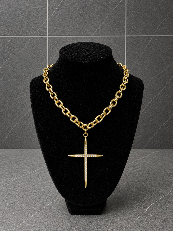 A gold chain necklace with a cross pendant displayed on a black velvet jewelry bust against a gray tiled background.